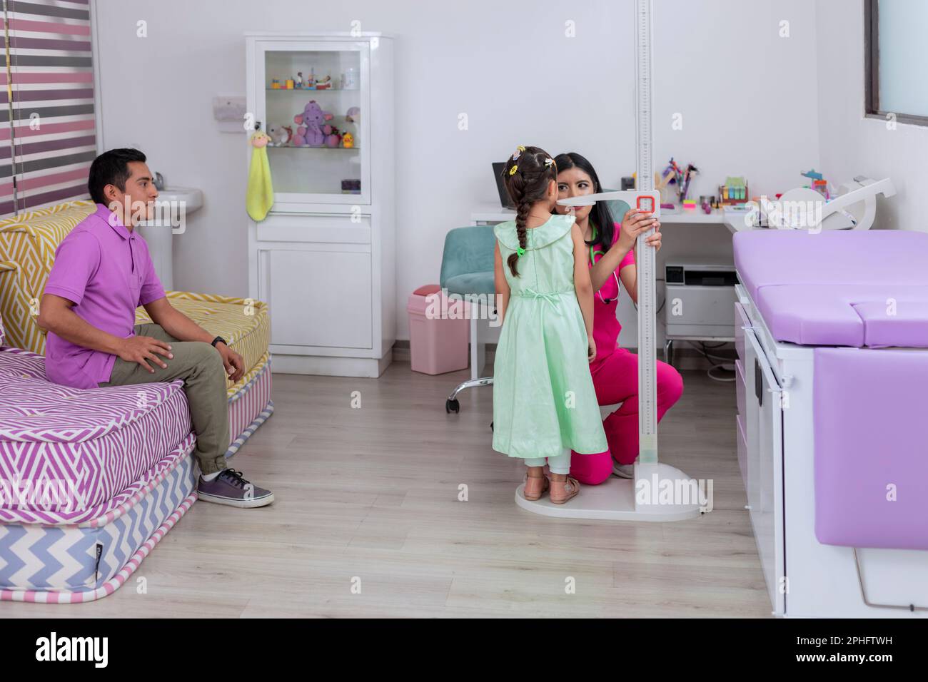Growth of a girl. Pediatrician doctor measuring the height of a little girl in her medical office, while her father watches them Stock Photo
