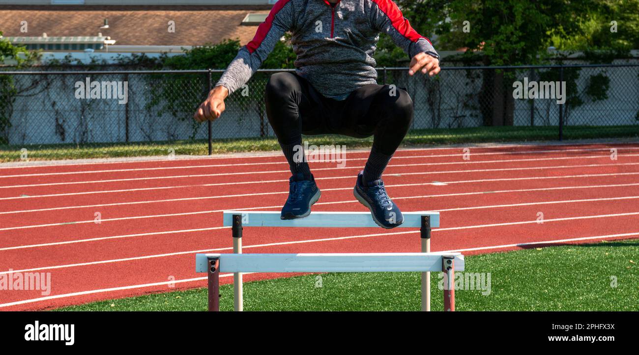 Front view of a high school boy jumping over track hurdles during track
