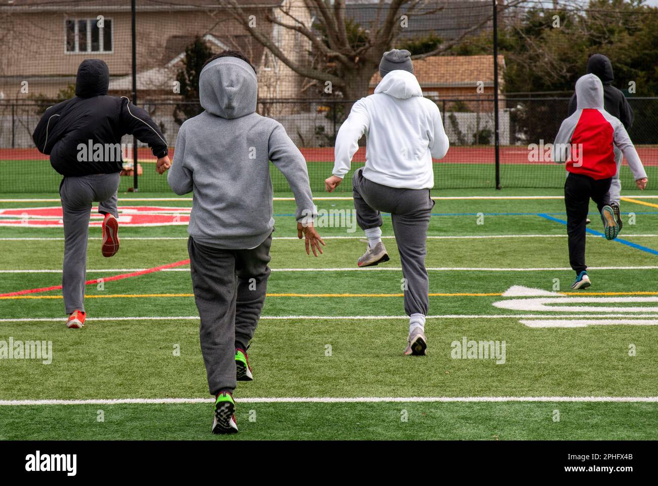 Rear view of rhigh school track unners performing speed sports drills on a turf field in the cold. Stock Photo