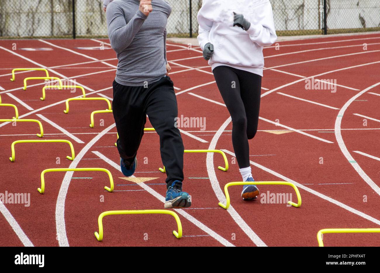 Two high school track runners running over yellow mini hurdles performing the wicket drill on a track druing practice. Stock Photo