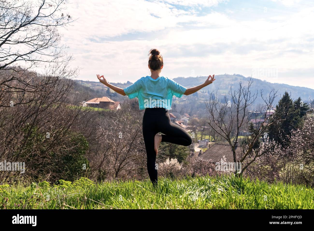 woman stands on hill in yoga pose against mountain and meditating 2PHFYJD