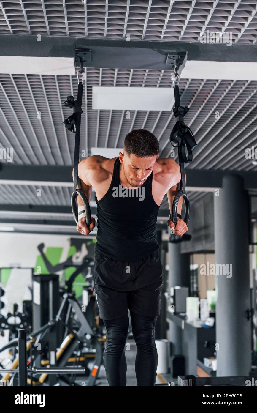 Strong Men Rinba Exercising on rings. Young sportive strong man in black wear have ...