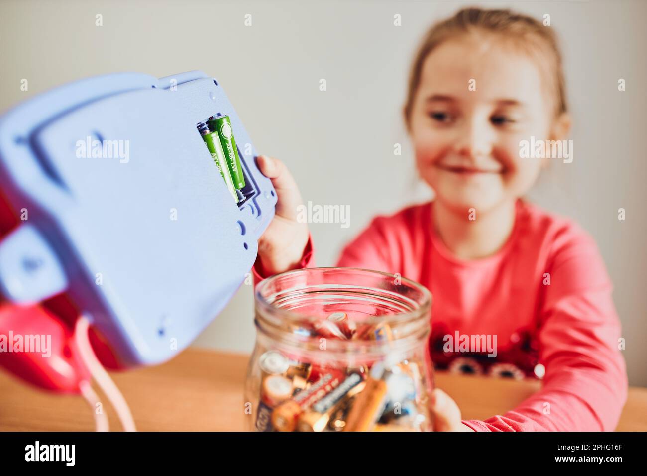 Little girl removing used batteries from toy and putting into jar for