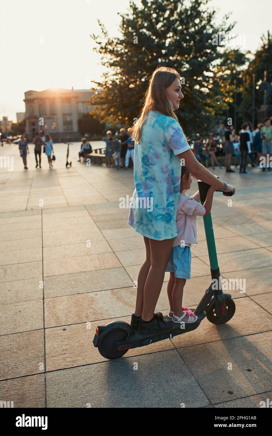 Teenager girl and her sister preschooler riding an electric scooter in ...