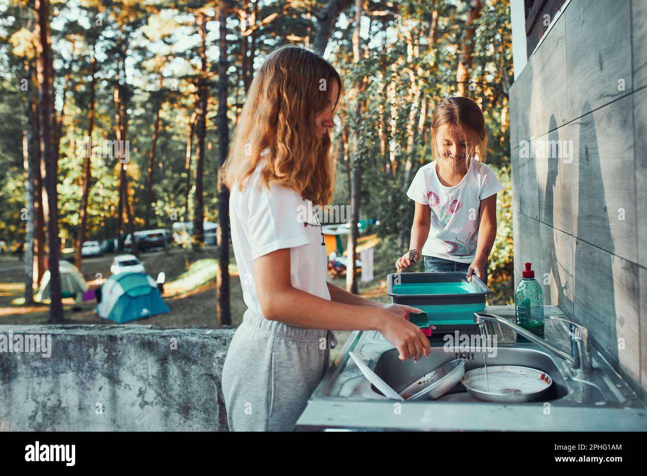Teenager girl washing up the dishes pots and plates with help her