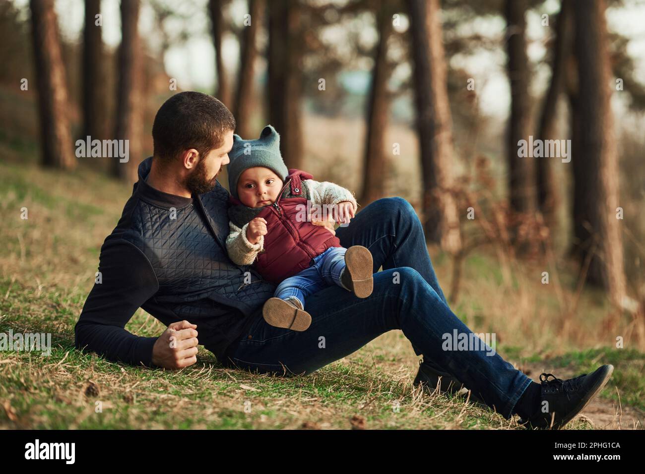 Father with his little son sitting on the ground in forest together ...