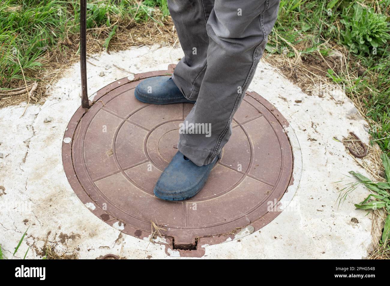 A man stands on the lid of a sewer well. Maintenance of sewerage and