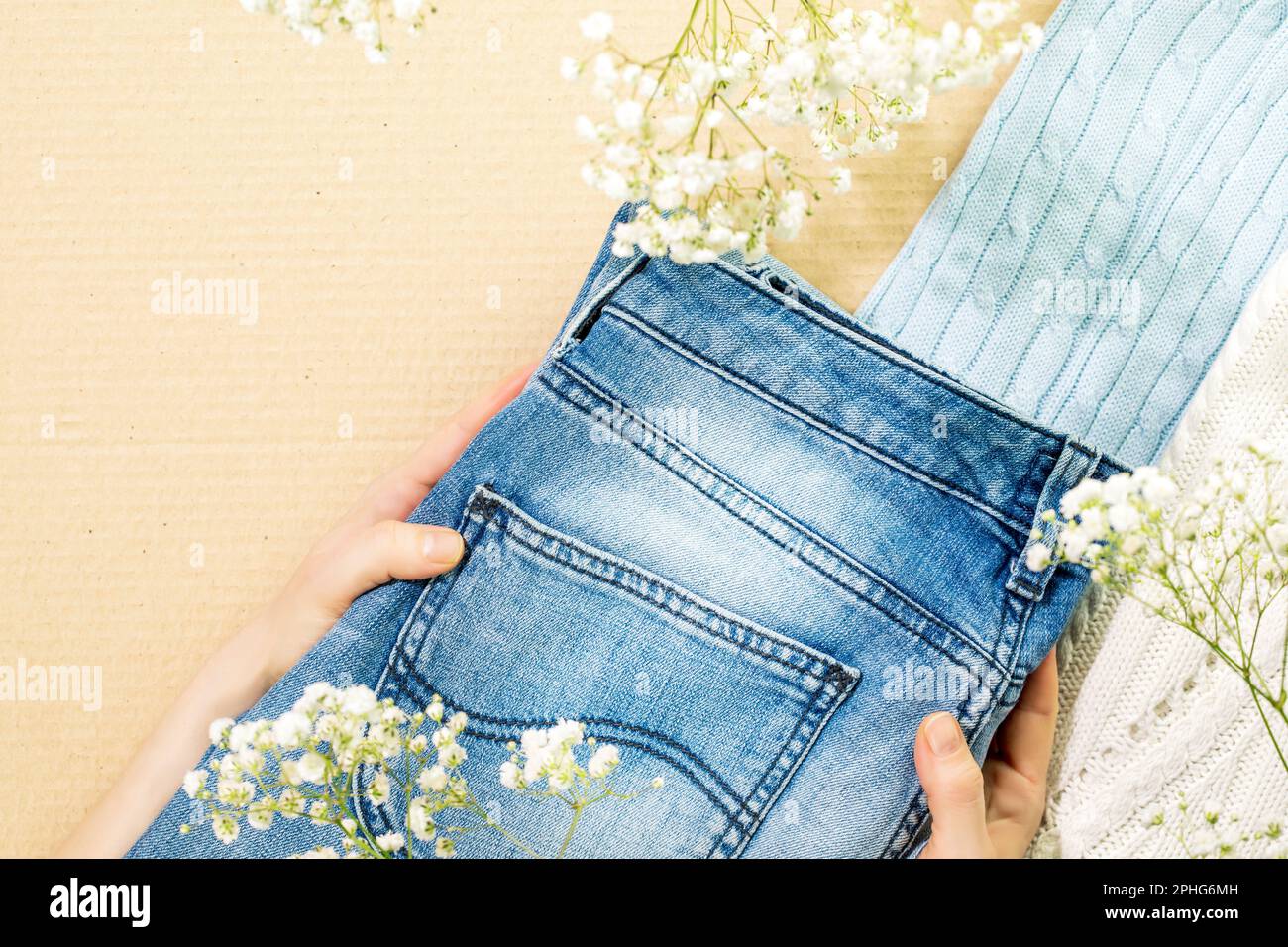Second hand concept. Sustainable life style with female hands holding jeans near sweaters on cardboard background. Circular fashion, eco friendly sust Stock Photo