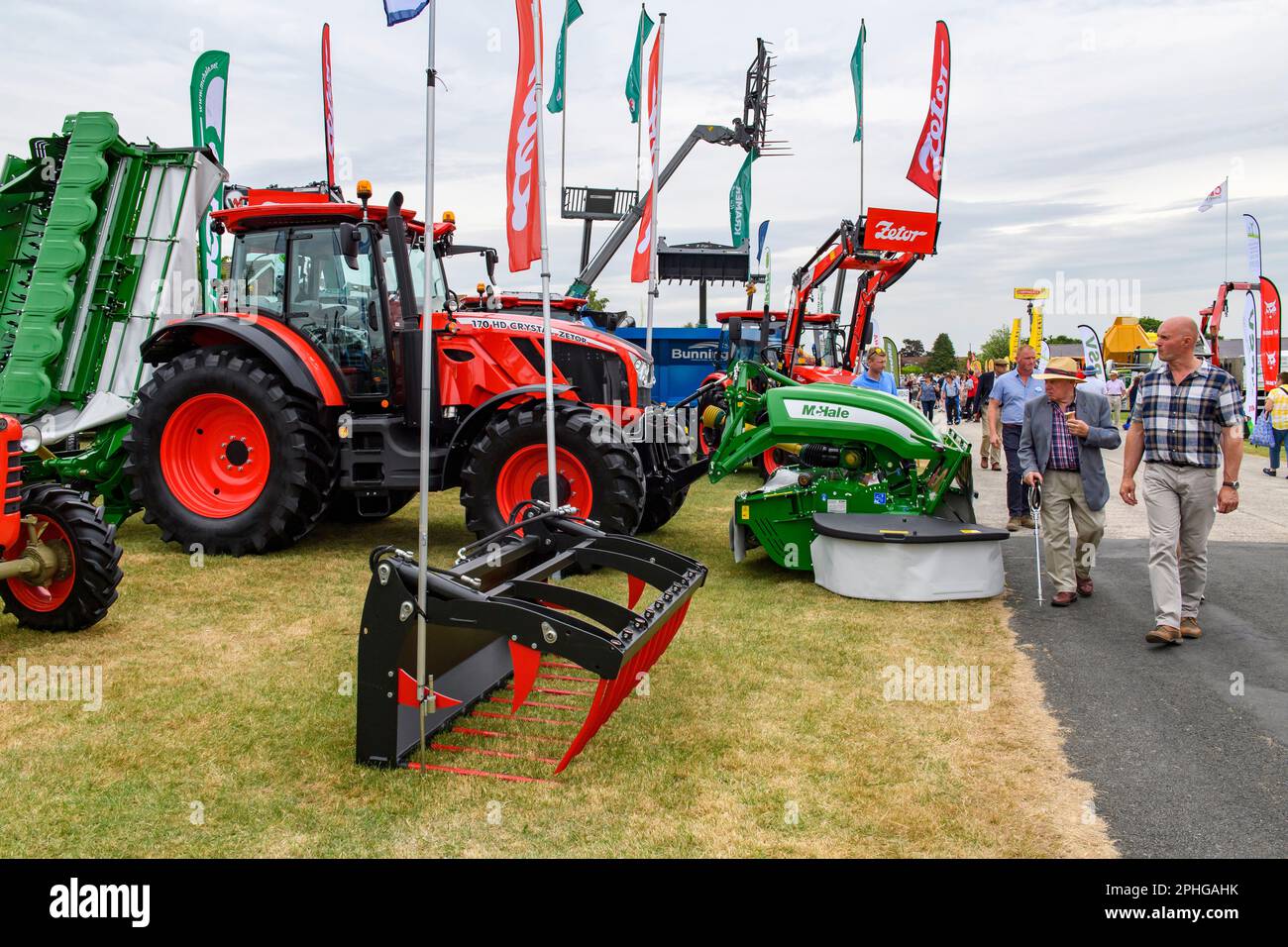 Agricultural machinery displayed on trade stand (people passing new Zetor tractors & front loader) - Great Yorkshire Show 2022, Harrogate, England UK. Stock Photo