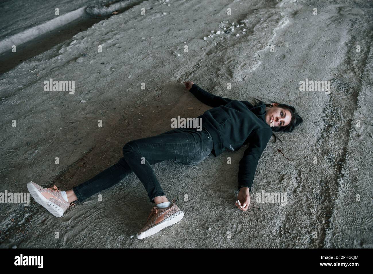 Corpse of female victim of crime lying down on the ground of abandoned building Stock Photo