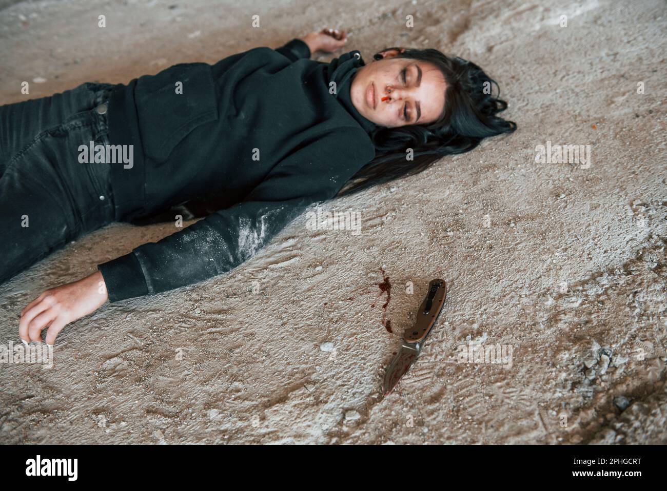 Corpse of female victim of crime lying down on the ground of abandoned building Stock Photo