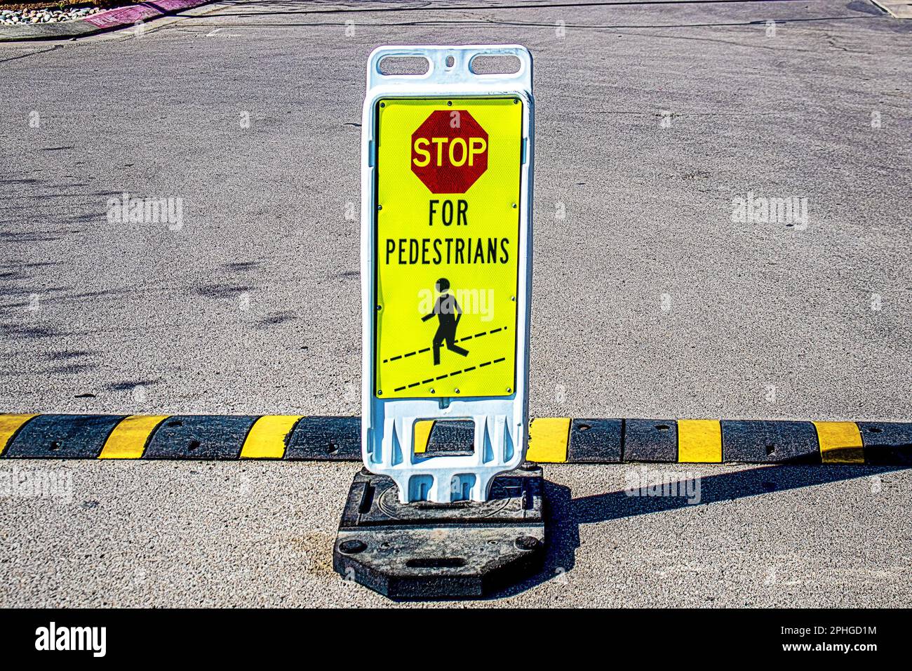 Weighted stand-up Stop for Pedestrians sign in grainy concrete parking lot by striped speed bump copy Stock Photo