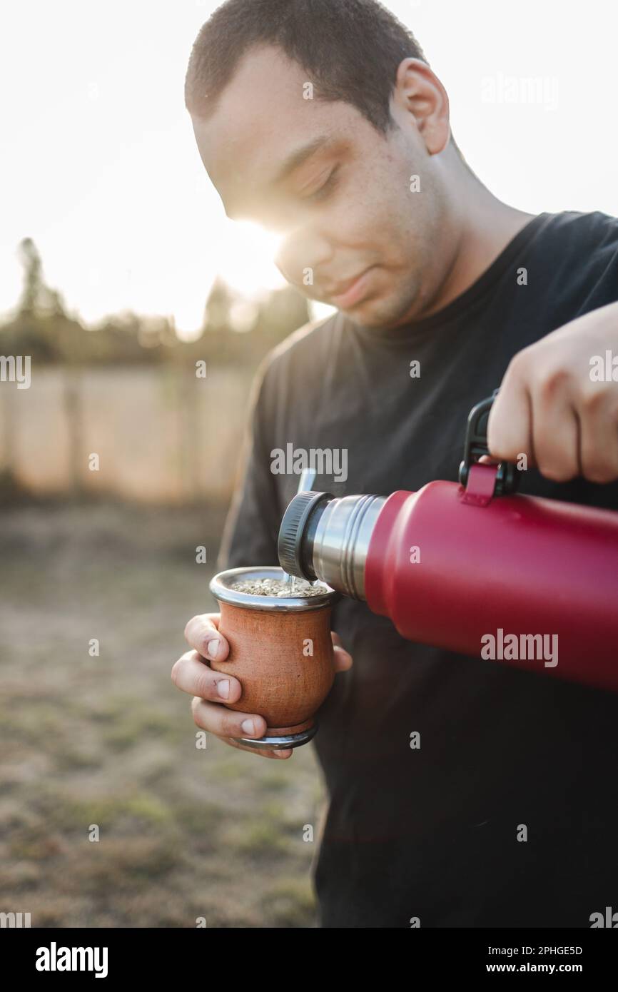 https://c8.alamy.com/comp/2PHGE5D/young-hispanic-man-brewing-yerba-mate-serving-hot-water-from-a-red-thermos-at-sunset-2PHGE5D.jpg