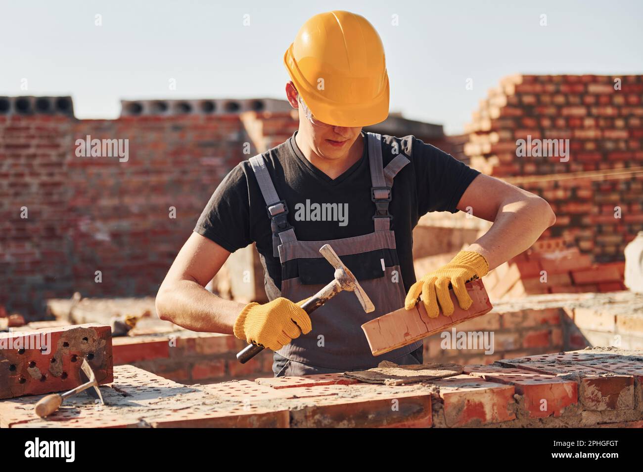 Holding brick and using hammer. Construction worker in uniform and