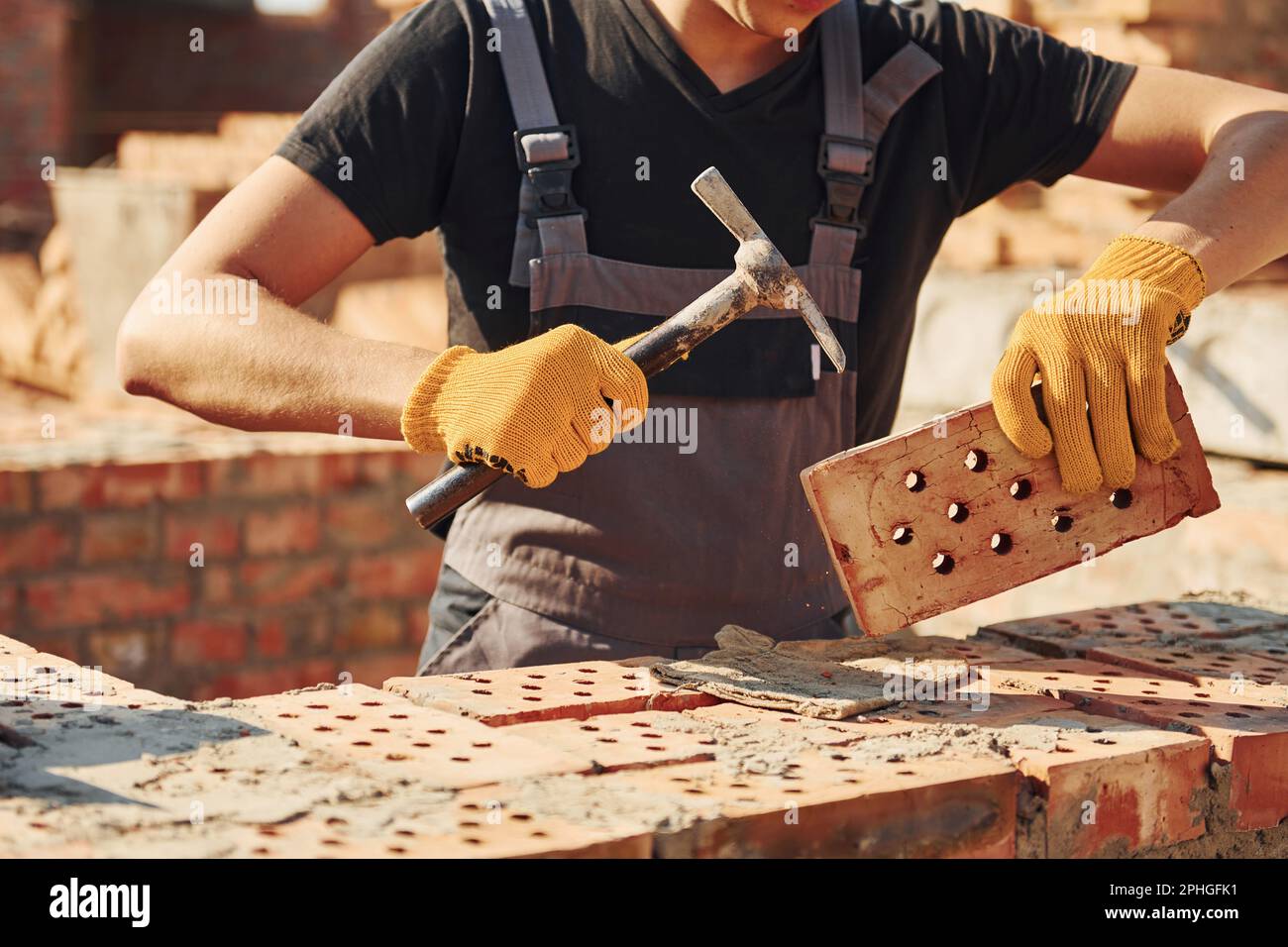 Holding brick and using hammer. Construction worker in uniform and