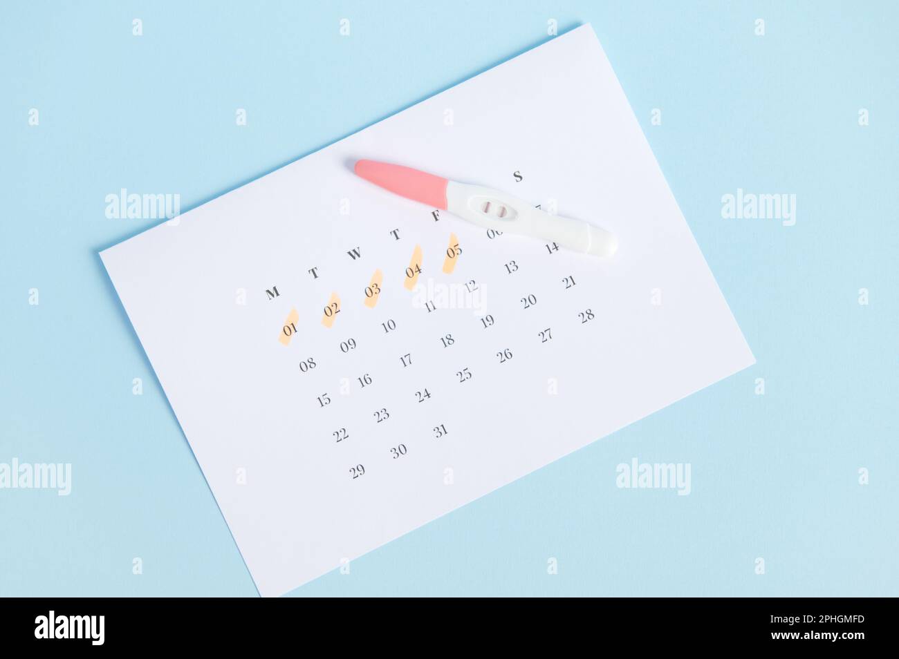 Top view positive pregnancy test on white calendar with last