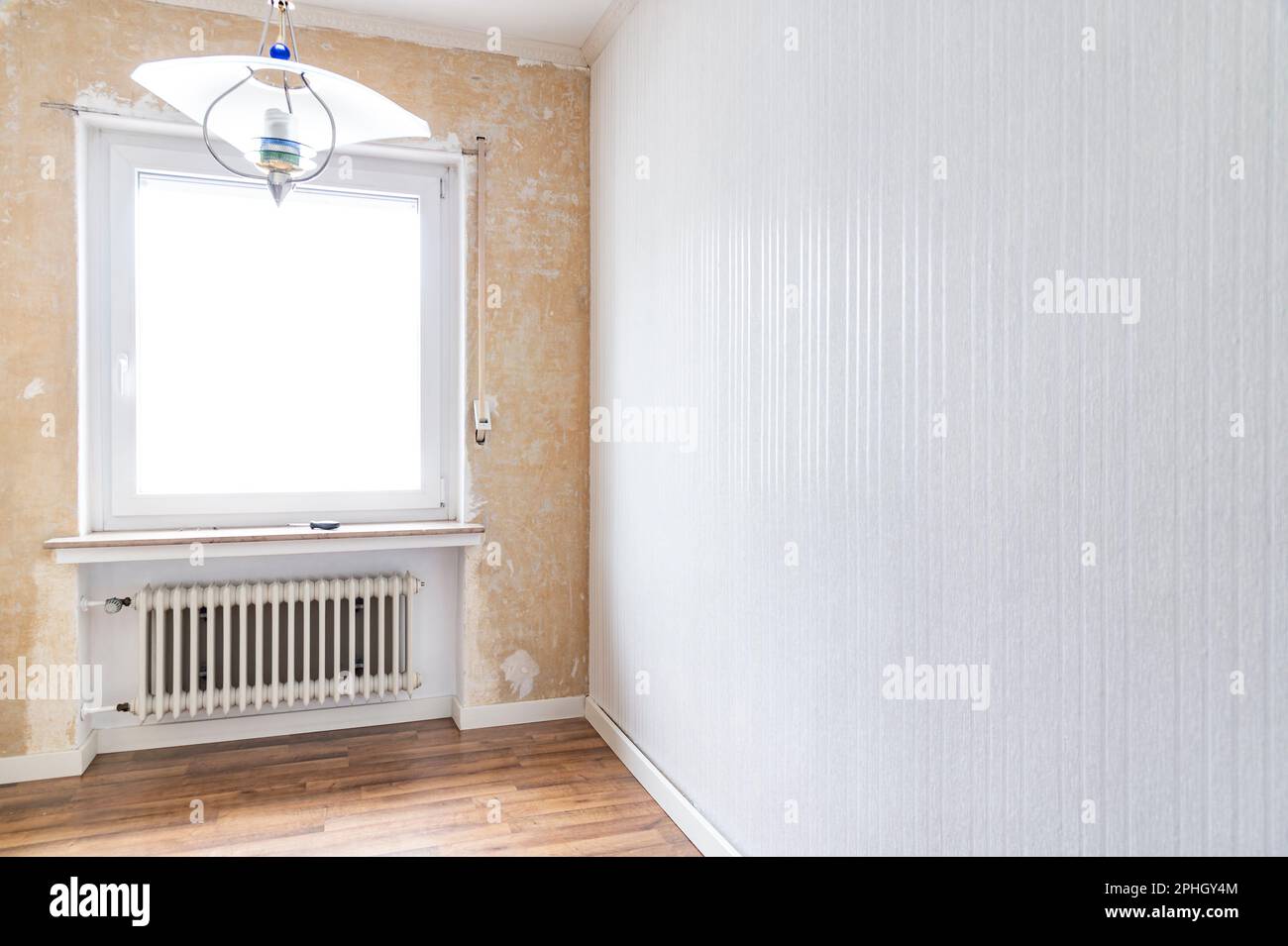 One room was partially renovated. The left side is still without wall covering. On the right, a new striped wallpaper was applied. Old ribbed radiator Stock Photo