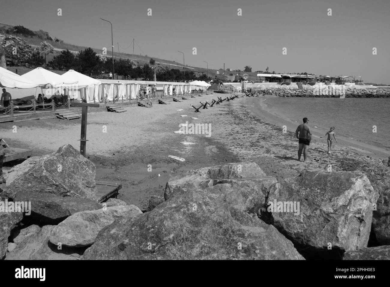 Odessa, Ukraine -2022: Metal military barriers, anti-tank hedgehogs on sea city beach. Vacationers sunbathe next to iron anti-tank hedgehogs. Fences f Stock Photo