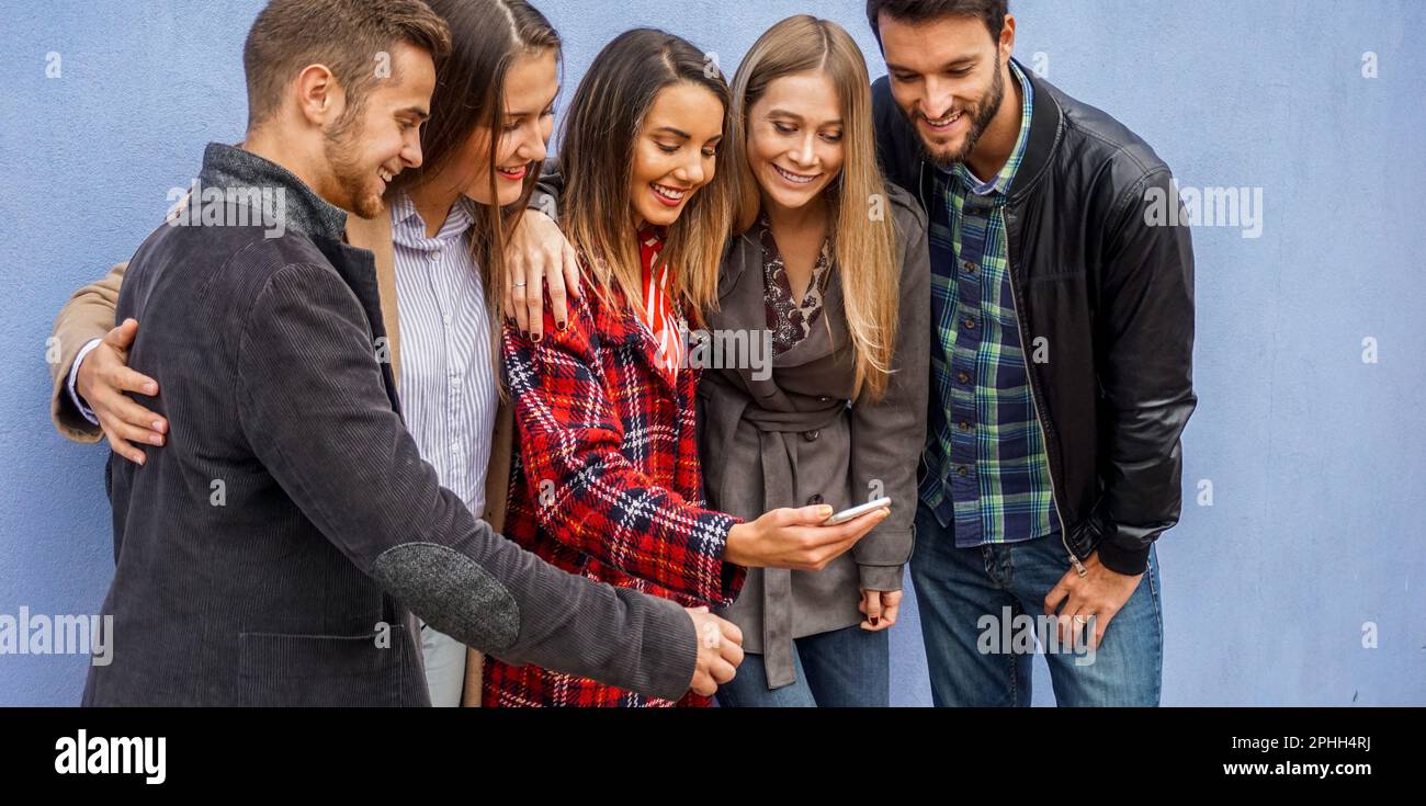 Group of people standing by the wall and sharing online stuff- Friends checking out their smartphones- Technology concept Stock Photo