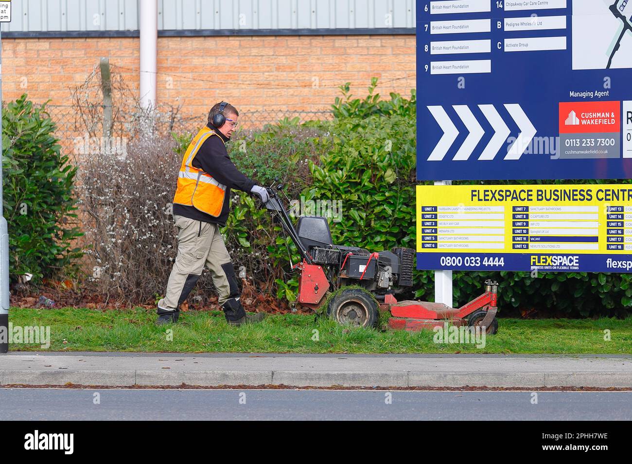 A gardener using a petrol lawn mower to cut grass on road side verges in an industrial estate in Leeds,West Yorkshire,UK Stock Photo
