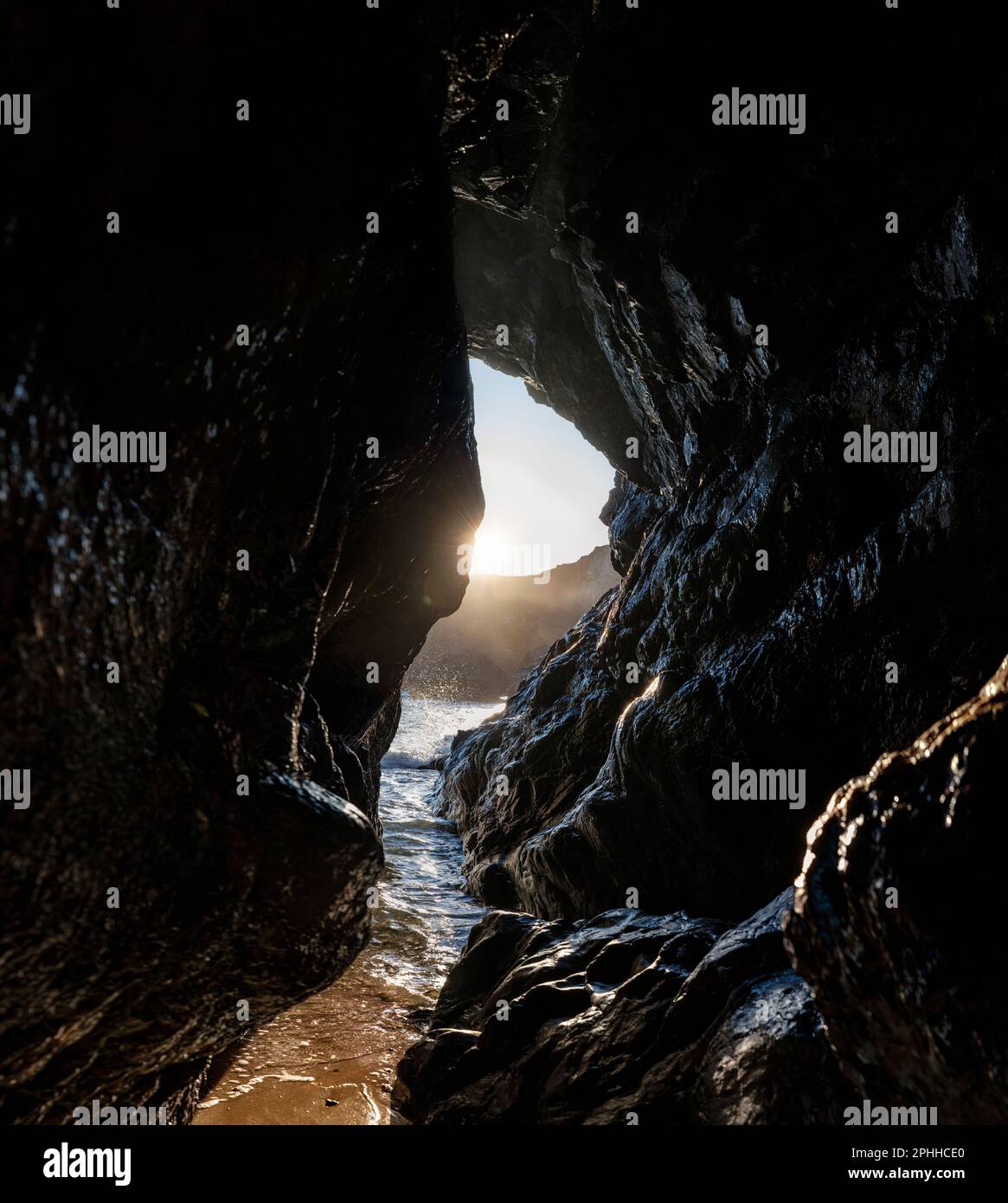 A sea cave at sunset through the rocks of Kynance Cove on the Lizard Peninsula, Cornwall, as the sun sets and the tide comes in. Stock Photo