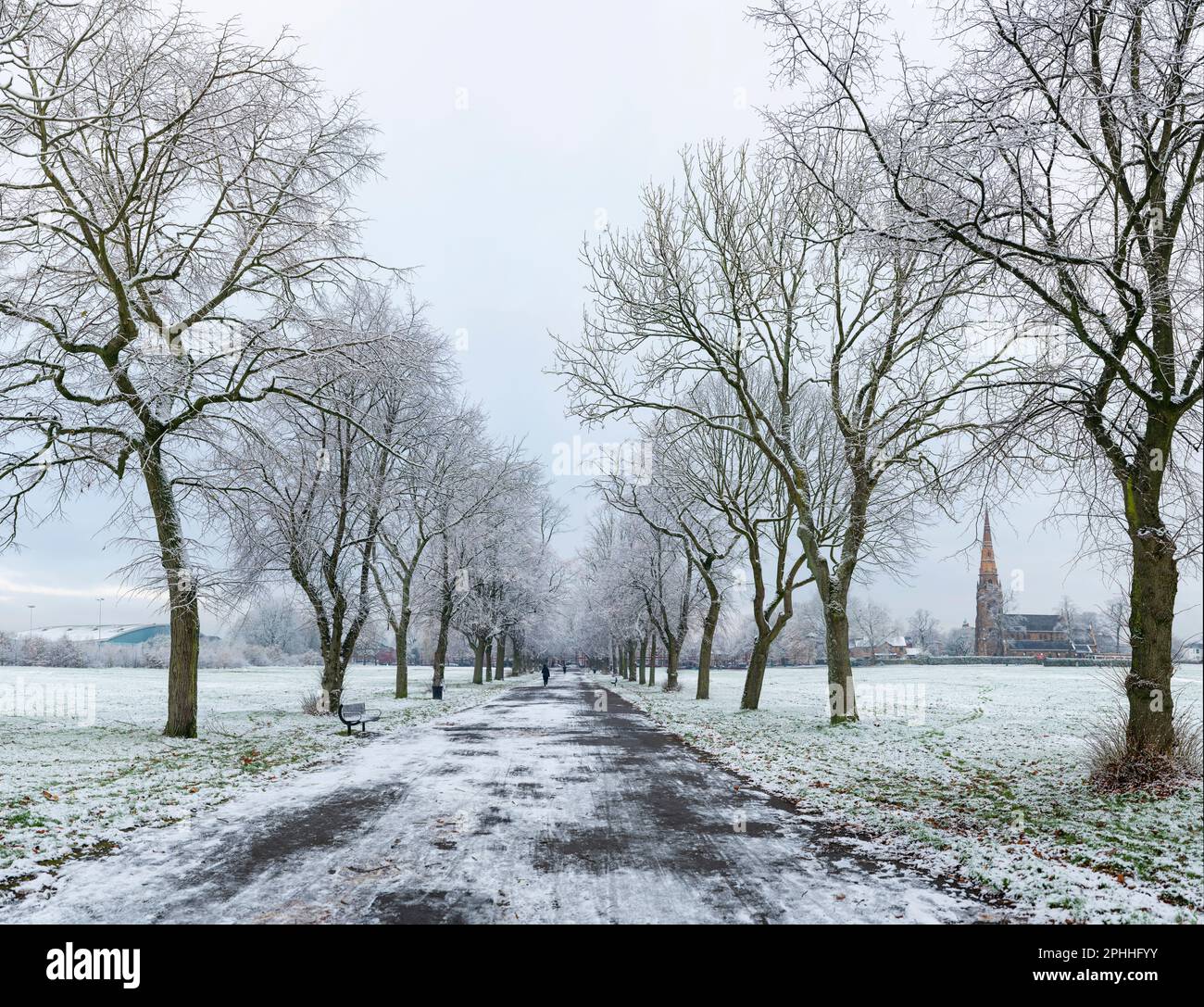 Avenue of trees in Platt Fields Park in South Manchester on a snowy and frosty winters morning, with the Holy Trinity Platt church in the distance. Stock Photo