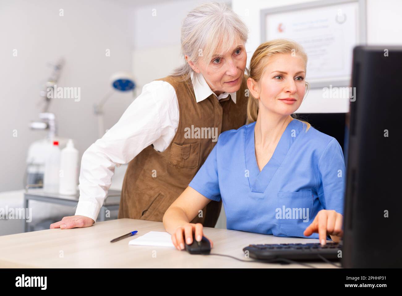 Interested elderly female client with cosmetologist looking at computer screen Stock Photo