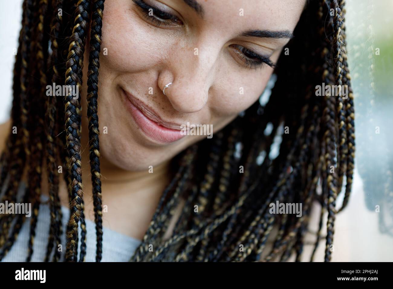 Closeup portrait of a girl holding back laughter, looking down. Focus on her small nose ring