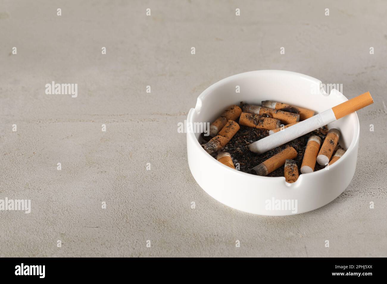White ceramic ashtray with cigarette butts on grey table. Space for text  Stock Photo