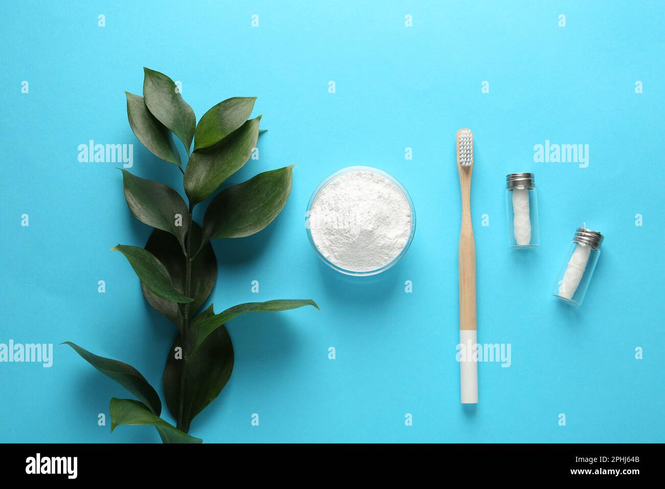 Bowl of tooth powder, brush, dental flosses and plant on turquoise