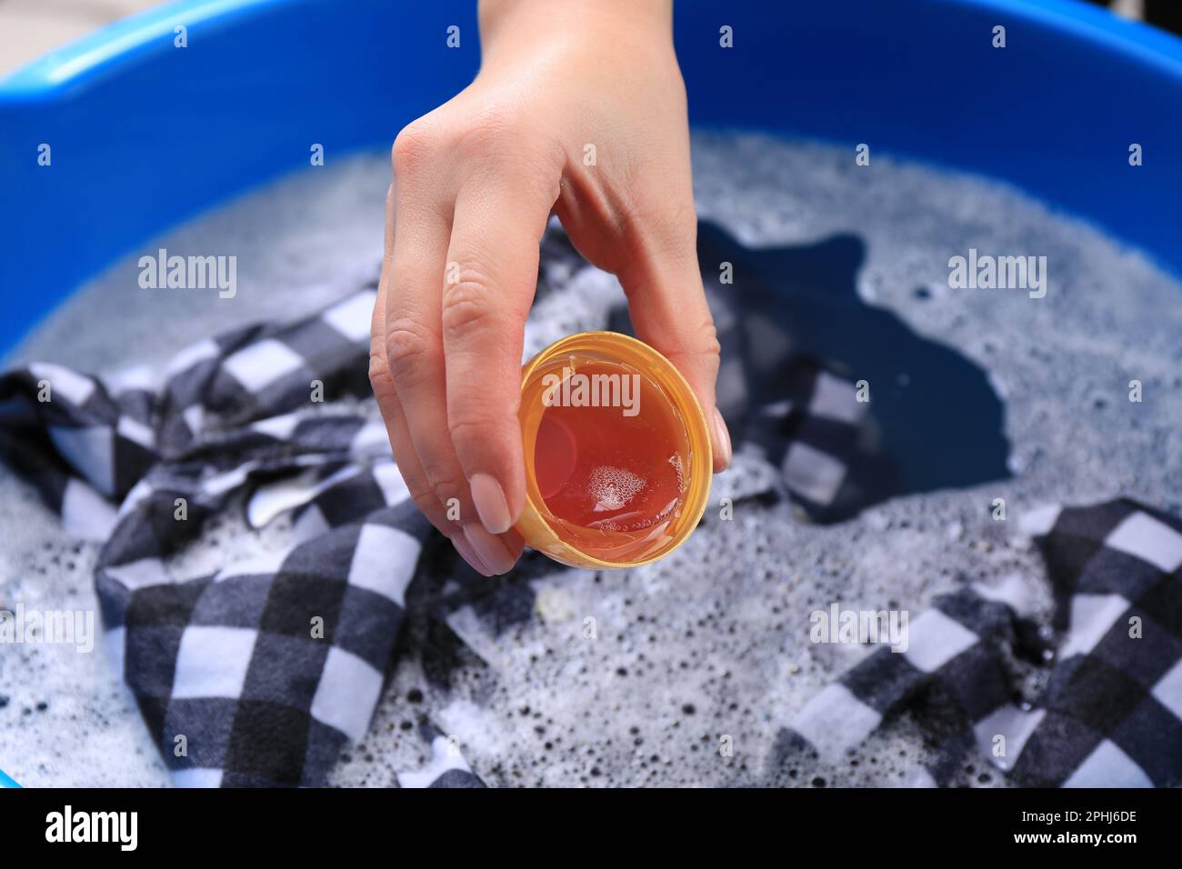 Woman pouring detergent into basin with clothing, closeup. Hand washing