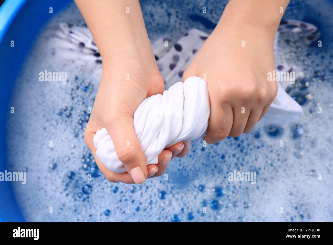 Woman wringing garment over basin, closeup. Hand washing laundry Stock