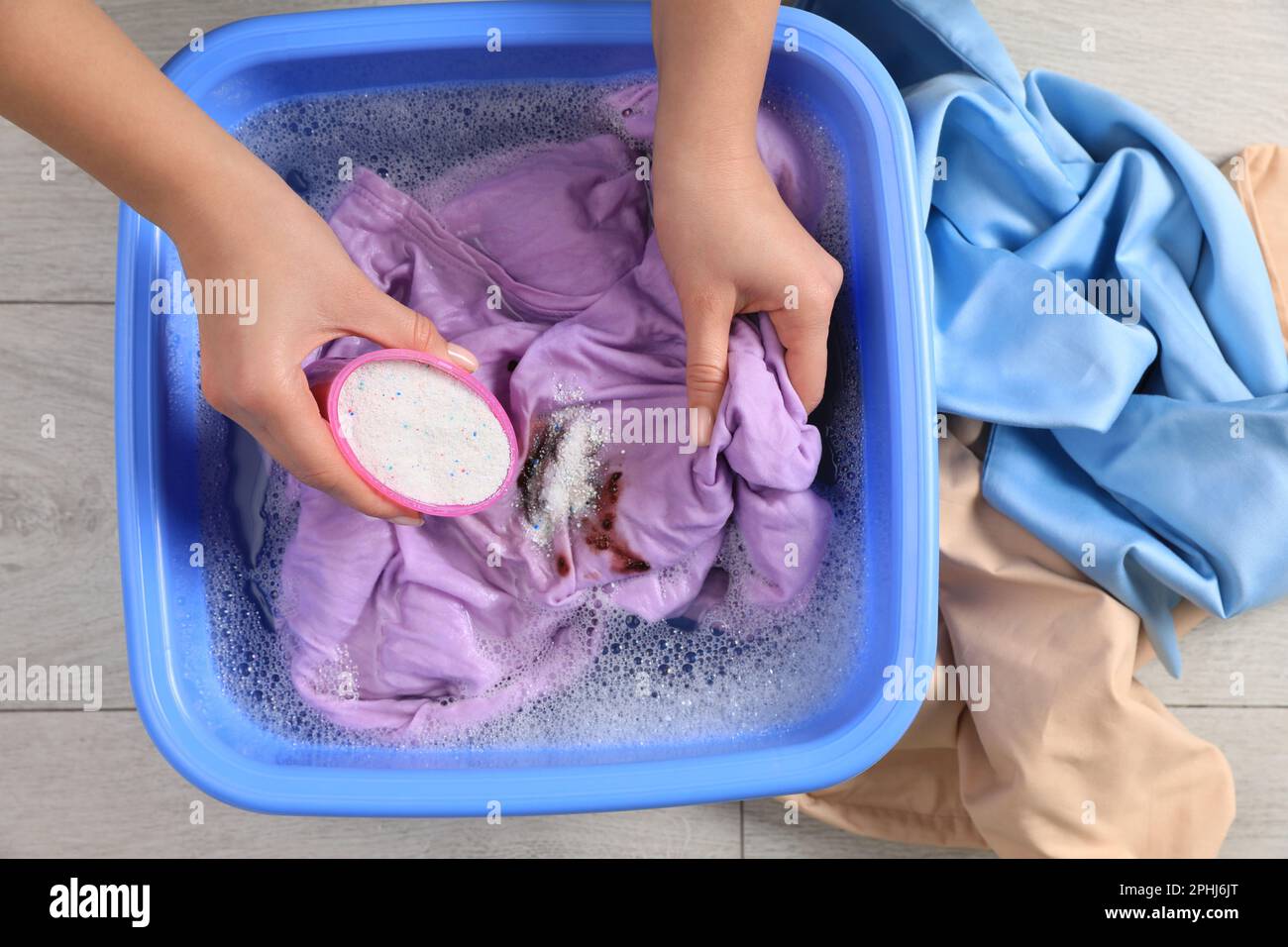 Woman adding powdered detergent into basin with clothes, top view. Hand
