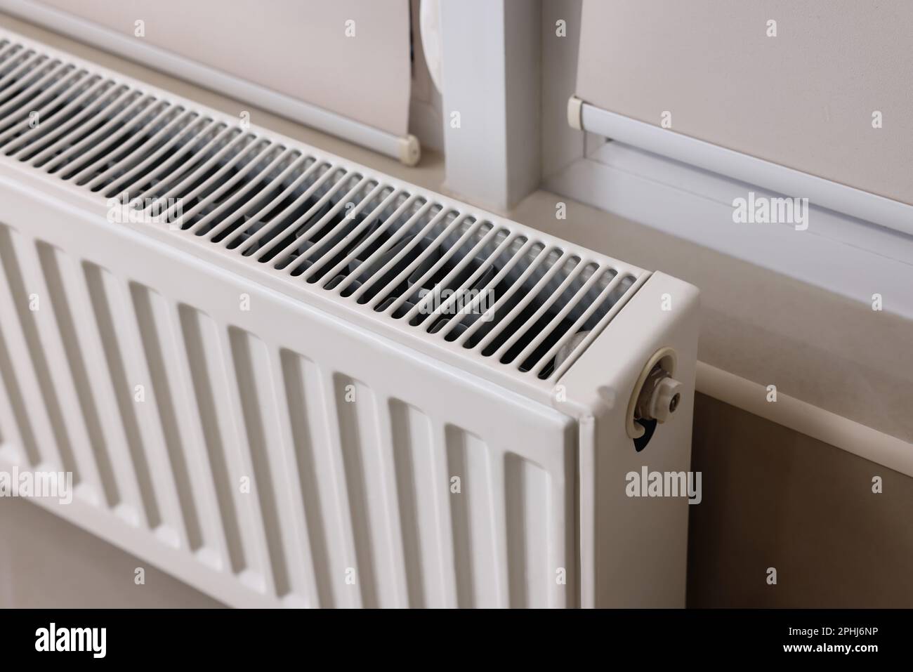 Modern radiator near window indoors, closeup. Central heating system