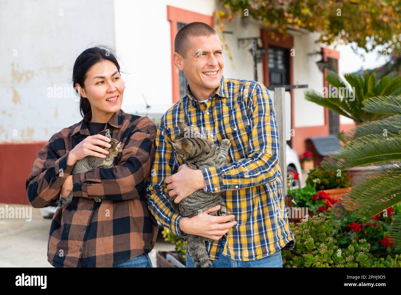 Man and woman with cats in their arms on the background of a country house Stock Photo