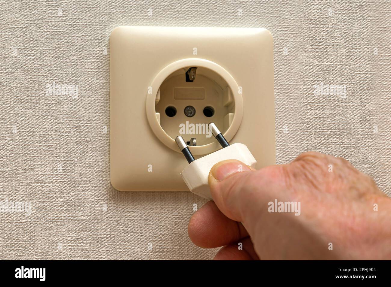 A person's hand pulls the plug out of an electrical outlet. Close up