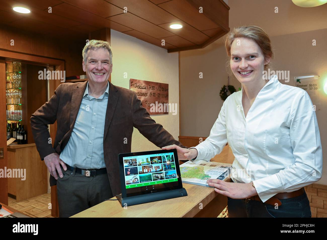 Waldeck, Germany. 22nd Mar, 2023. Christian Gerlach, owner of the Hotel Werbetal in the district of Nieder-Werbe, stands at the reception next to his daughter Lisa Kalhöfer, whose hand is on a tablet. Even before the Corona pandemic, the owner and his family equipped the 28 rooms of his hotel with tablets and Internet-enabled TVs. Bookings in the restaurant are thus possible at any time, and there is also a stable WLAN network on the terrace. (to dpa 'Are hotels and restaurants in Hesse being left behind digitally?') Credit: Uwe Zucchi/dpa/Alamy Live News Stock Photo