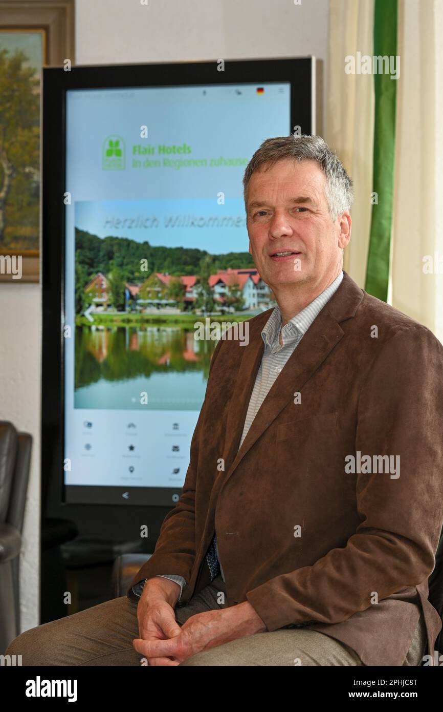 Waldeck, Germany. 22nd Mar, 2023. Christian Gerlach, owner of the Hotel Werbetal in the district of Nieder-Werbe, sits in front of a digital information board in the entrance area. Even before the Corona pandemic, the owner and his family equipped the 28 rooms of his hotel with tablets and Internet-enabled TVs. Bookings in the restaurant are thus possible at any time, and there is also a stable WLAN network on the terrace. (to dpa 'Are hotels and restaurants in Hesse being left behind digitally?') Credit: Uwe Zucchi/dpa/Alamy Live News Stock Photo