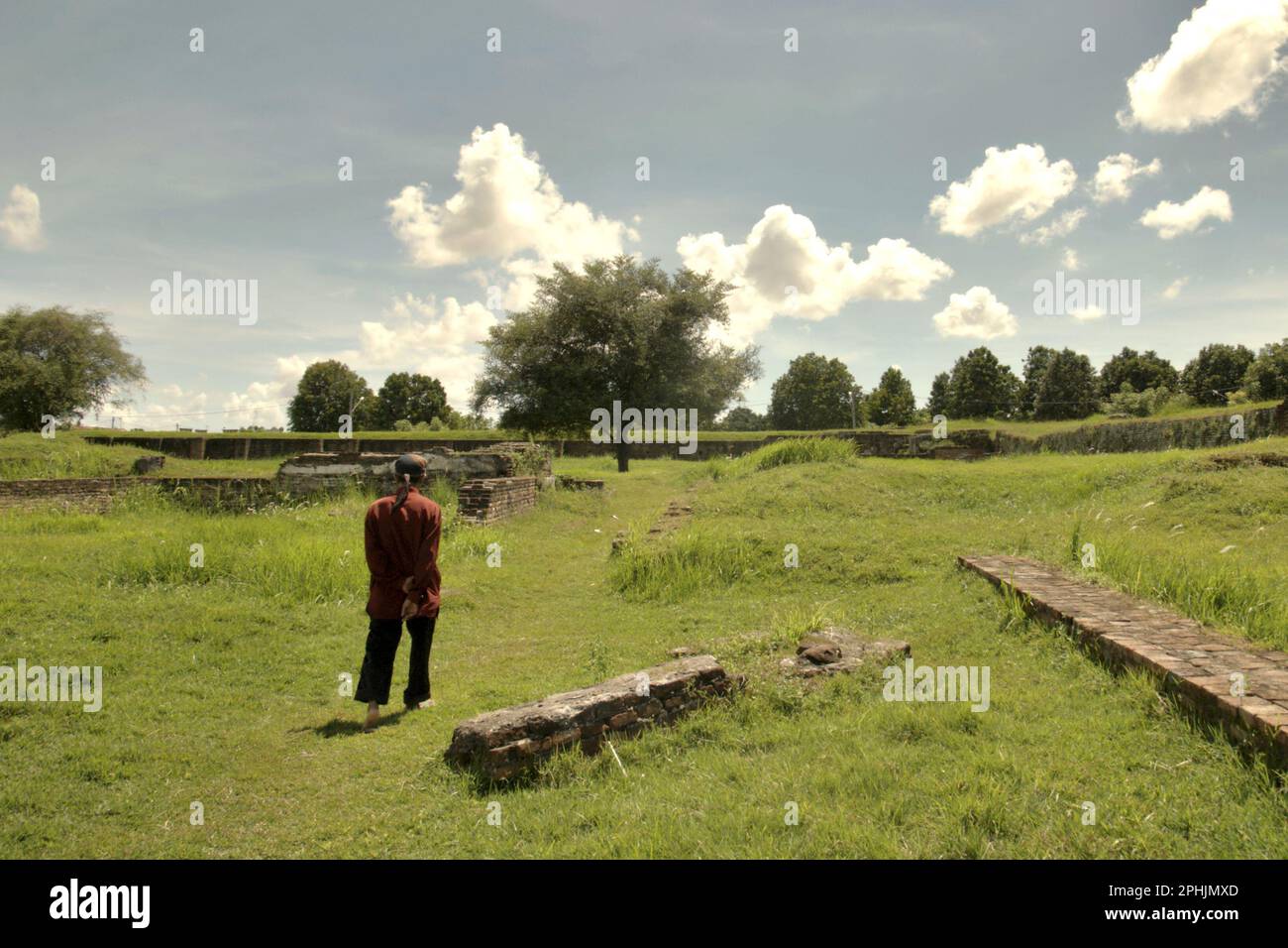 A man is walking through grassland in the middle of Surosowan Palace, a cultural heritage from Banten Sultanate period located in an area now called Banten Lama (Old Banten) in Serang, Banten, Indonesia, on this photo taken in 2010. 'The sustainability of cultural heritage is strongly linked to the effective participation of local communities in the conservation and management of these resources,' according to a team of scientists led by Sunday Oladipo Oladeji in their research article published on Sage Journals on October 28, 2022. Banten Lama (Old Banten) area was a part of the important... Stock Photo