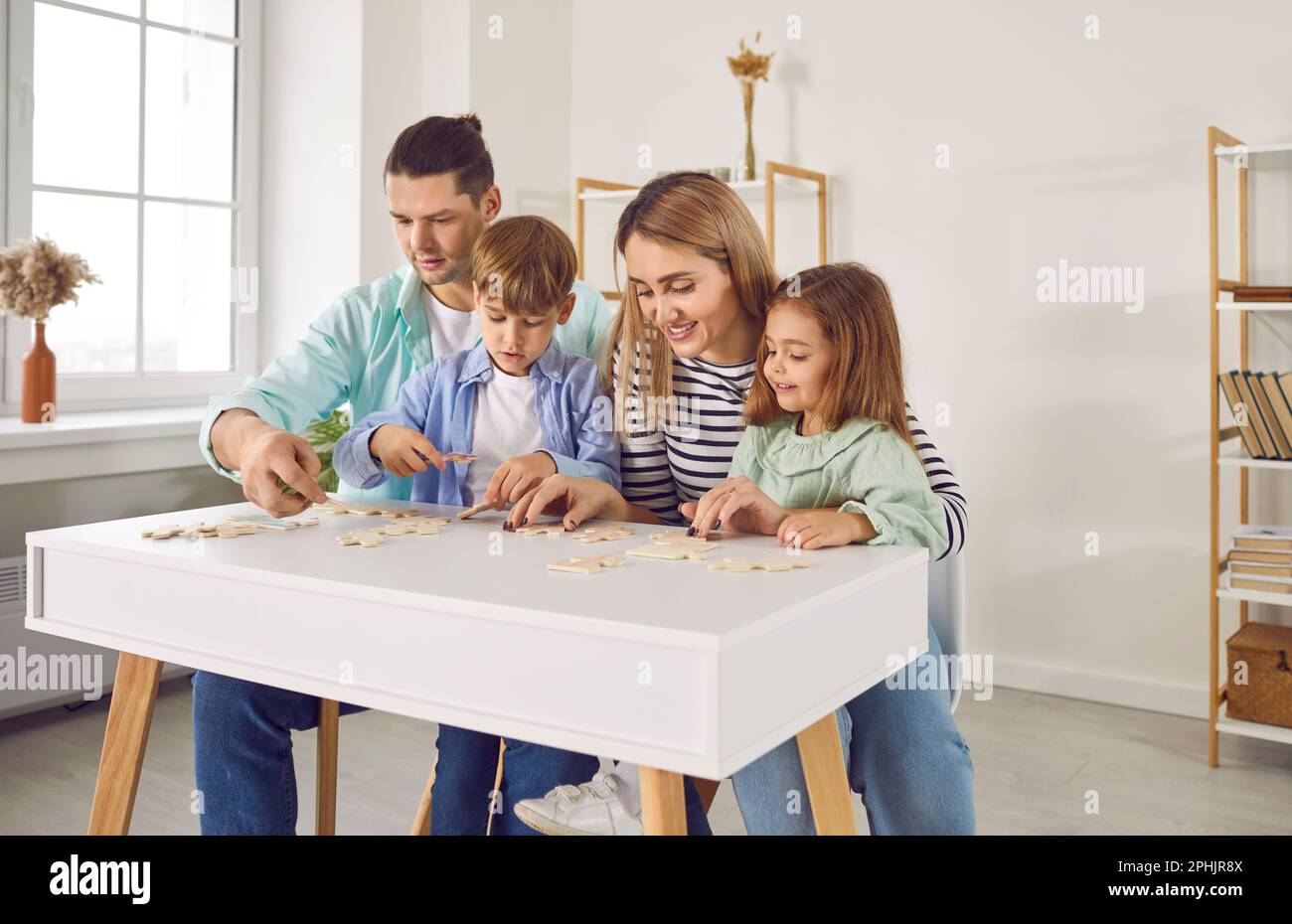 Parents playing with two kids in a puzzle in the living room at home. Stock Photo