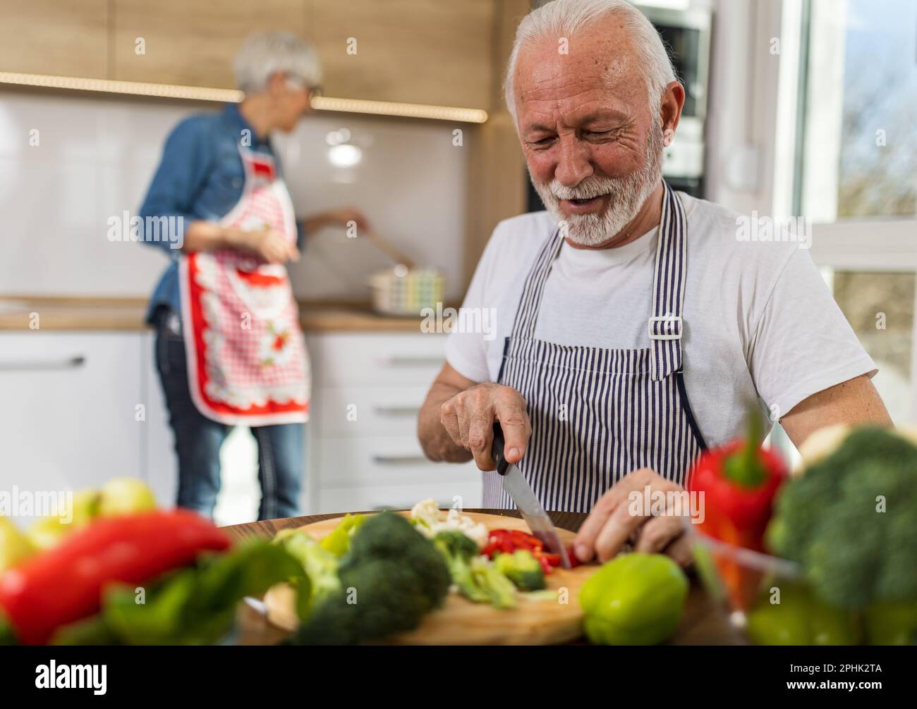 Senior couple preparing soup, husband cutting vegetable while wife cooking in background Stock Photo