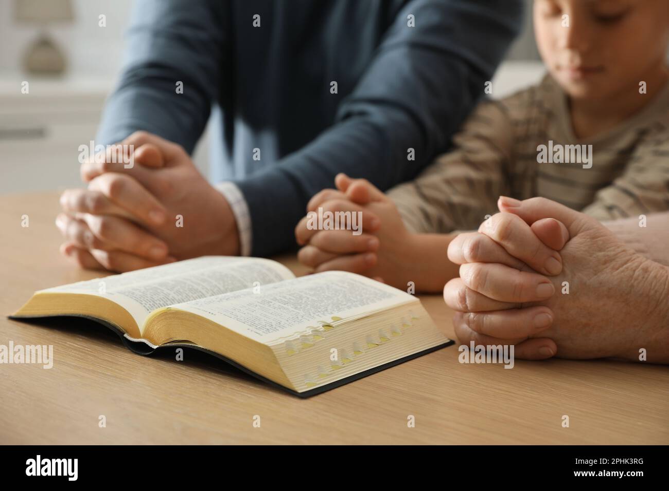 Boy and his godparents praying together at wooden table indoors, closeup Stock Photo
