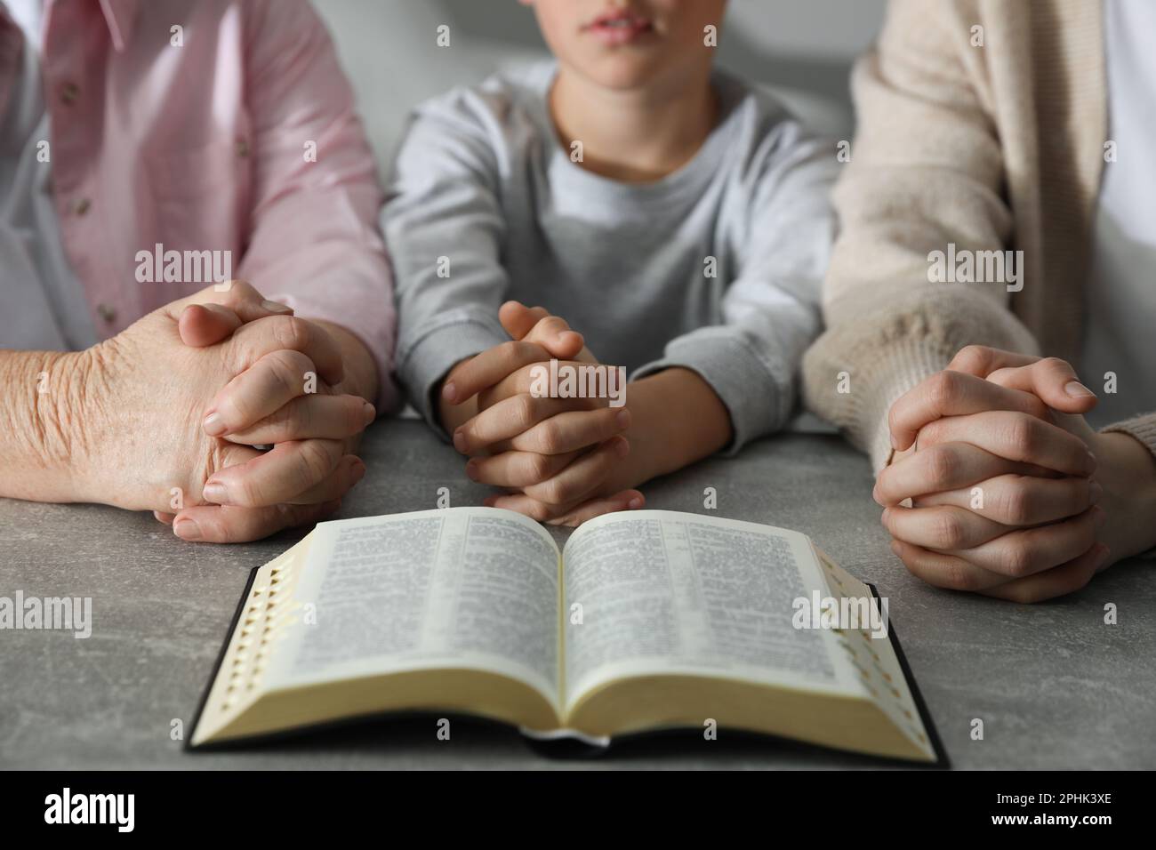 Boy and his godparents praying together at grey table, closeup Stock Photo