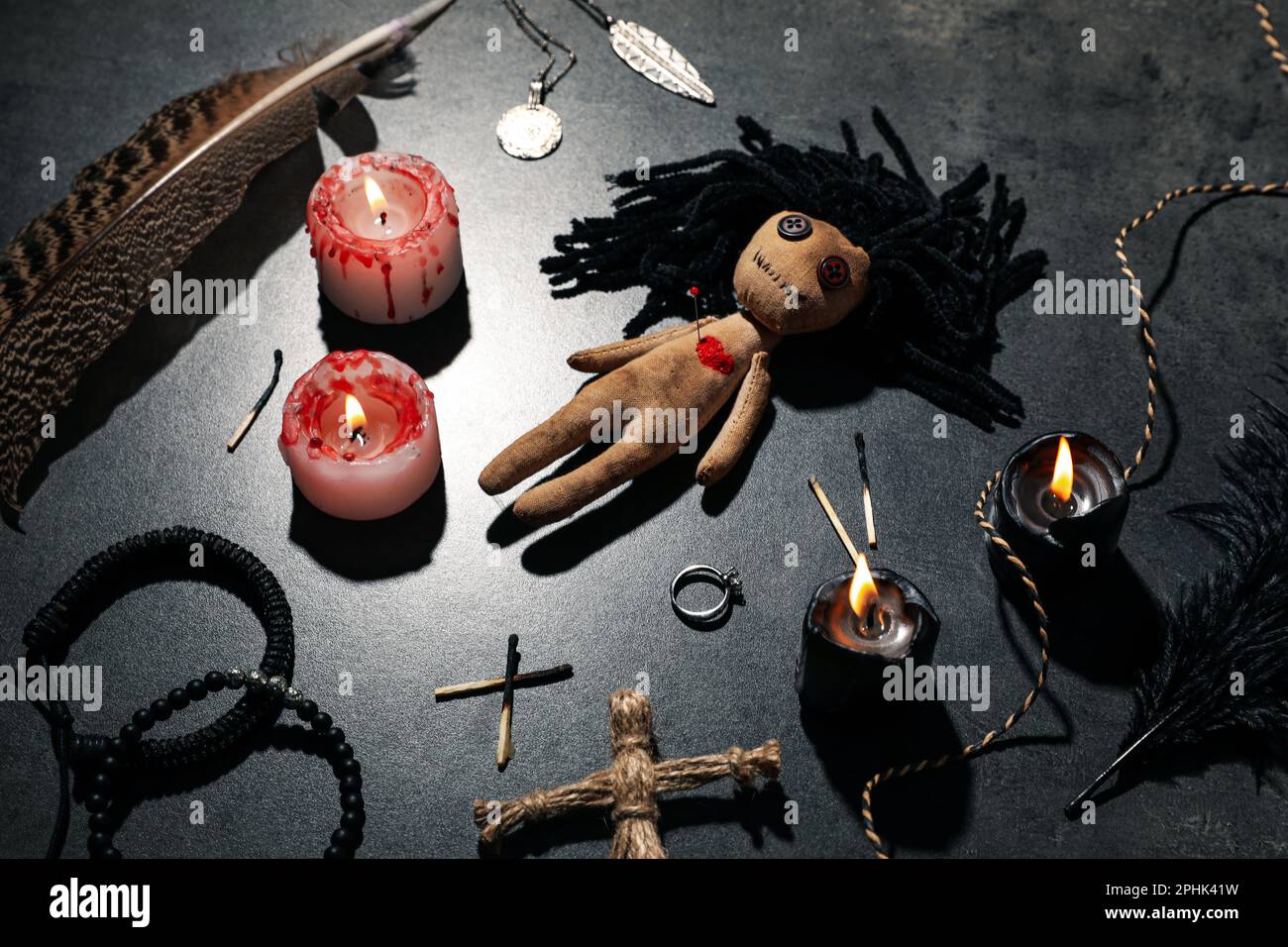 Female voodoo doll with pin in heart and ceremonial items on grey table ...