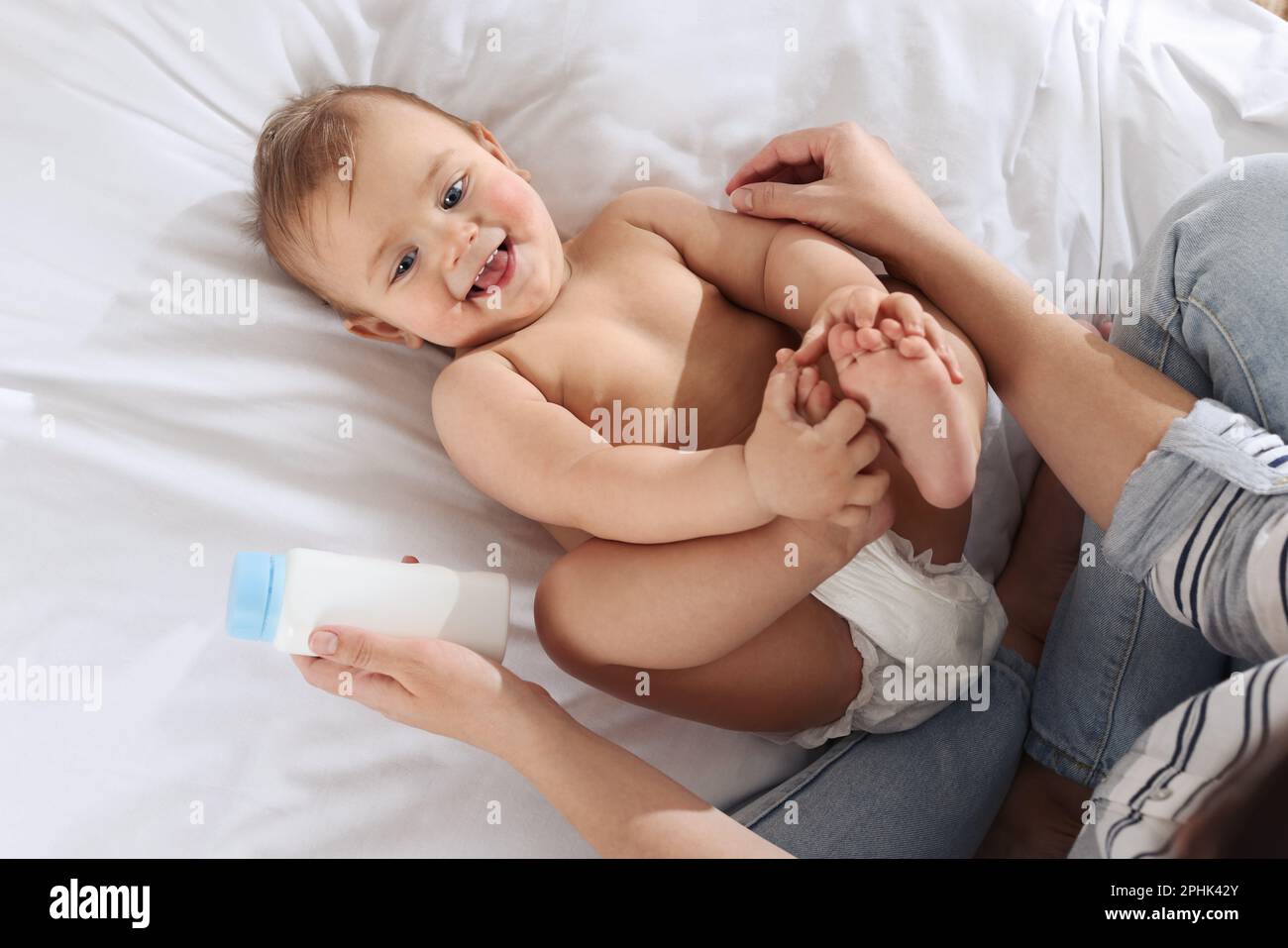 Mother with bottle of dusting powder near her cute baby on bed, top ...