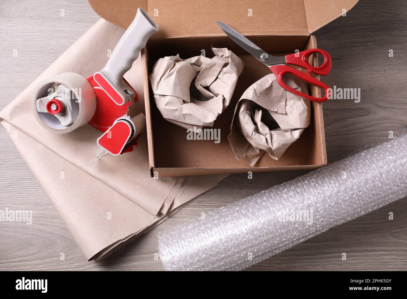https://c8.alamy.com/comp/2PHK5GY/open-box-with-wrapped-items-adhesive-tape-scissors-paper-and-bubble-wrap-on-wooden-table-flat-lay-2PHK5GY.jpg