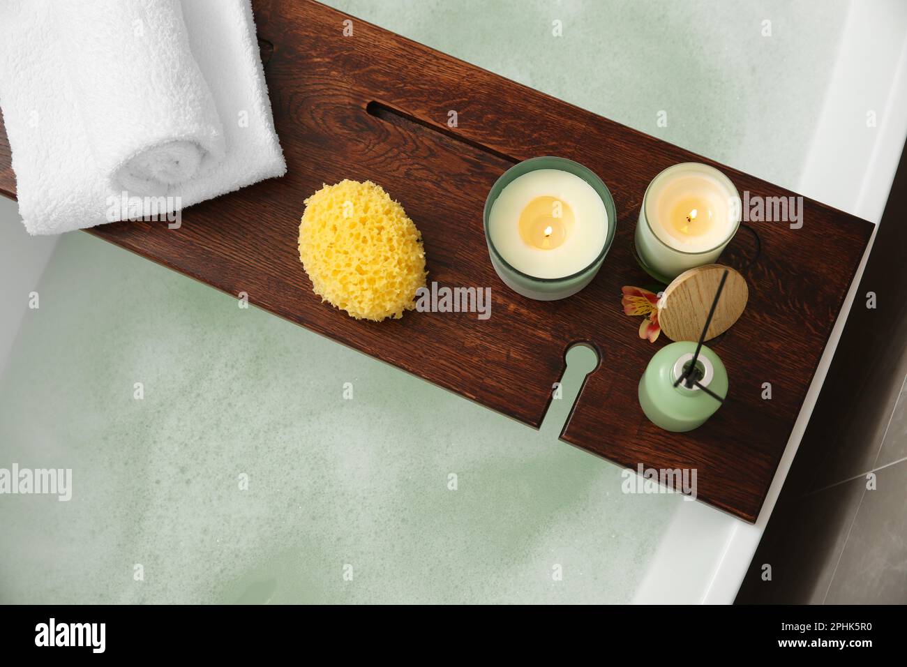 Wooden bath tray with candles, air freshener, towels and sponge on tub