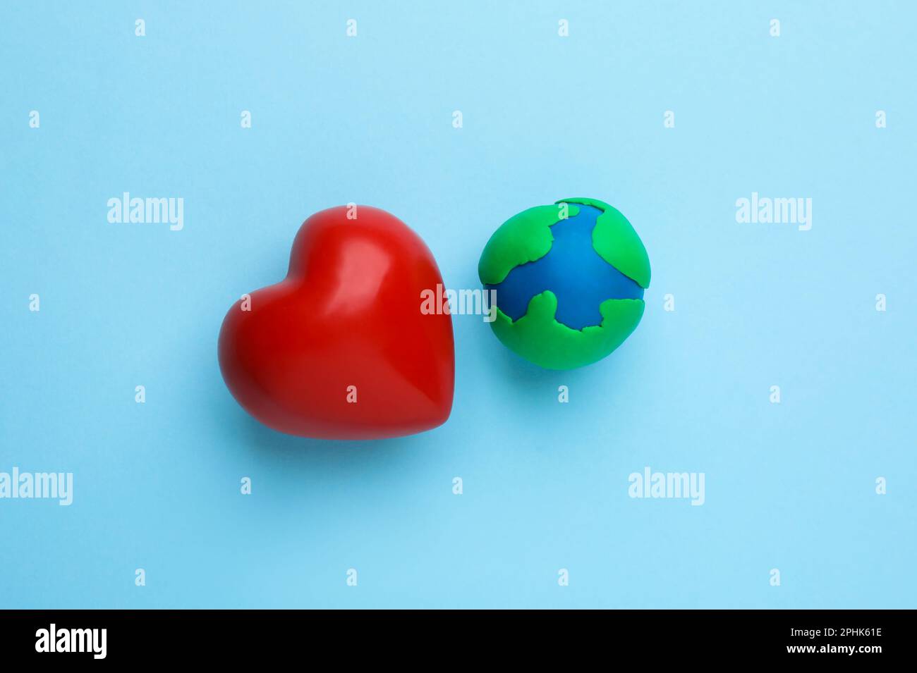Plasticine model of planet and red heart on light blue background, flat