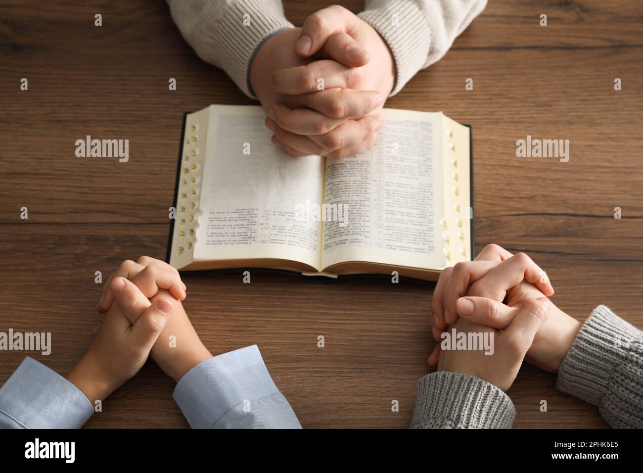 Boy and his godparents praying together at wooden table, closeup Stock Photo