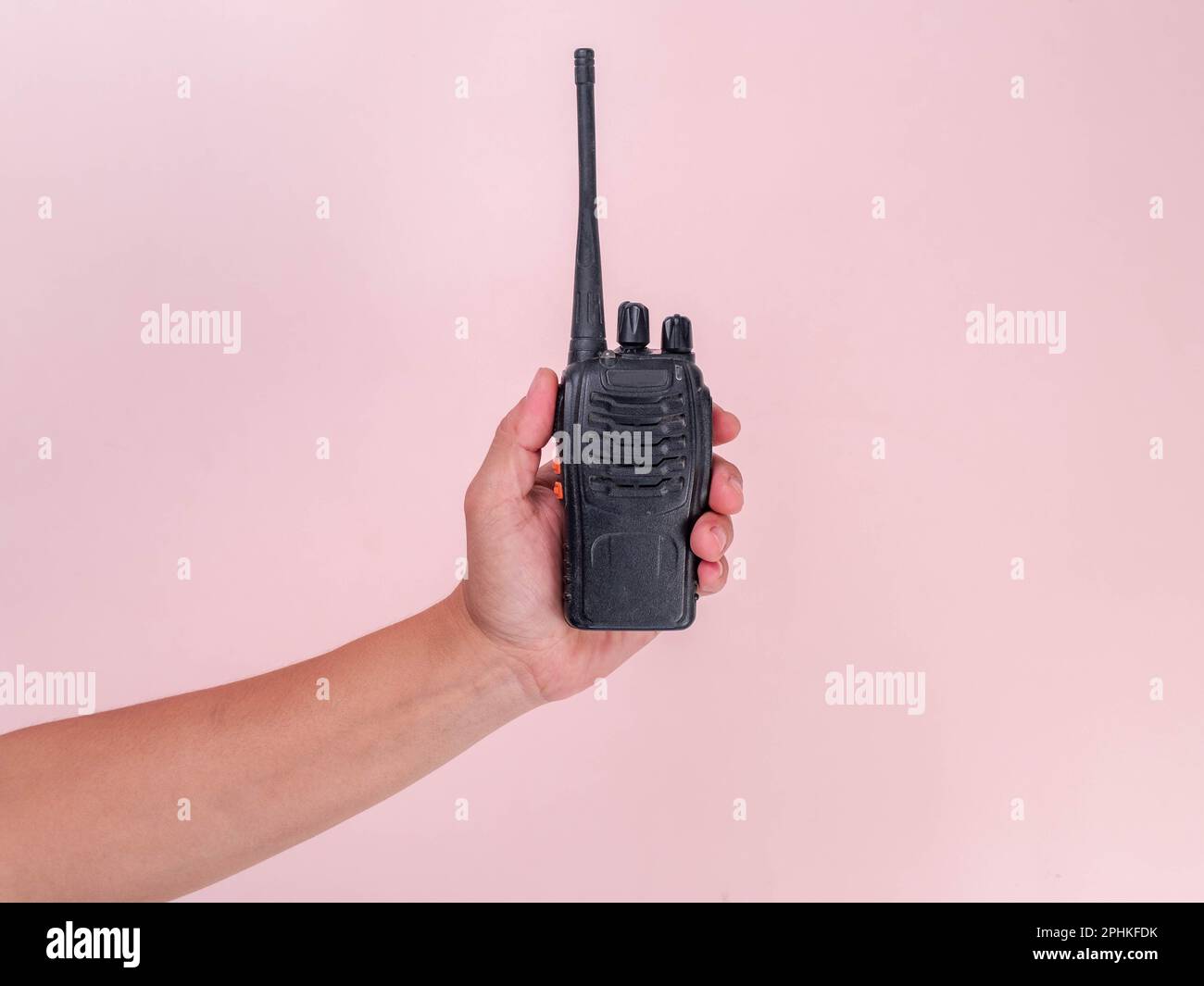 Close up hand holding portable walkie talkie isolated on pink background. Black handheld walkie talkie Stock Photo